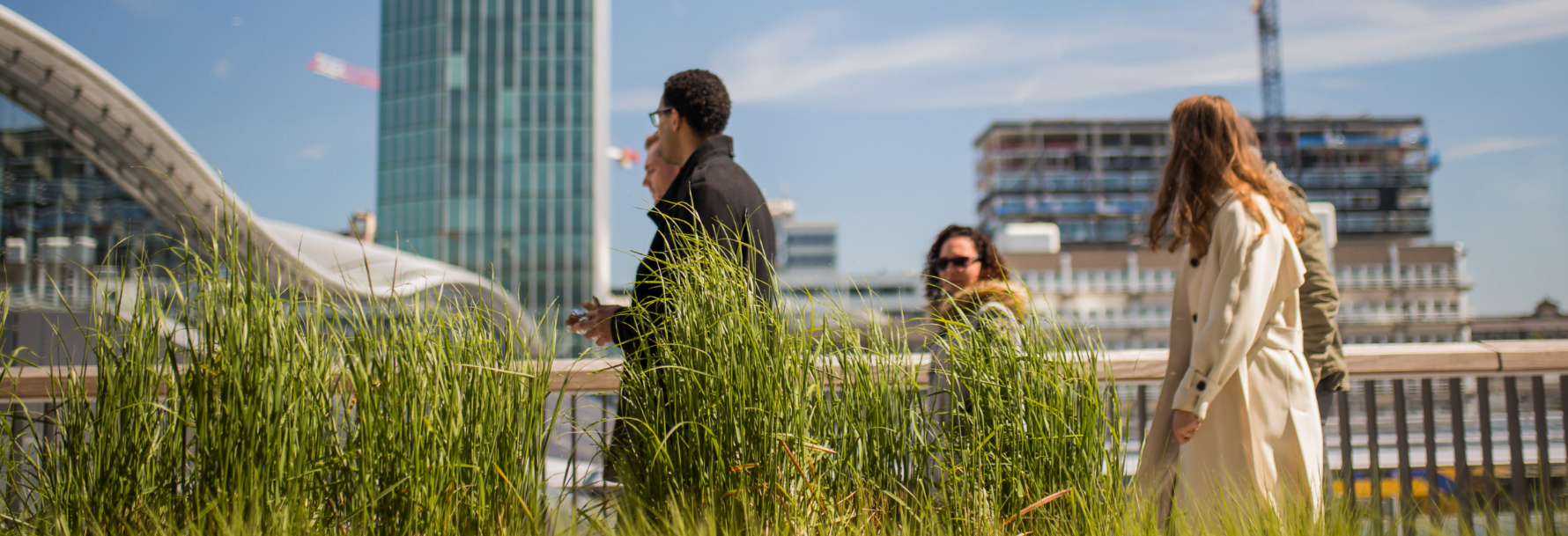 Groepje mensen wandelend mensen over de Moreelsebrug, met planten aan de voorgrond, Station Utrecht Centraal op de achtergrond.