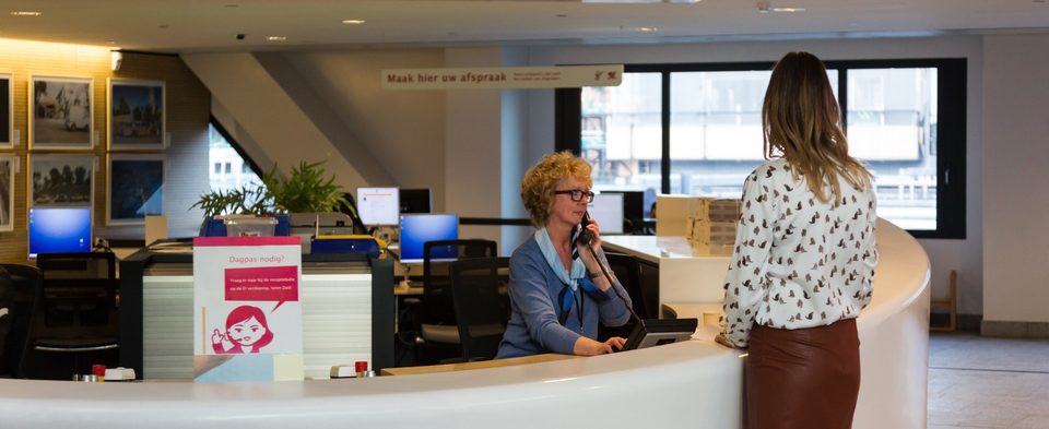 ontvangstbalie in het stadskantoor met een dame die achter de balie zit en een klant te woord staat.