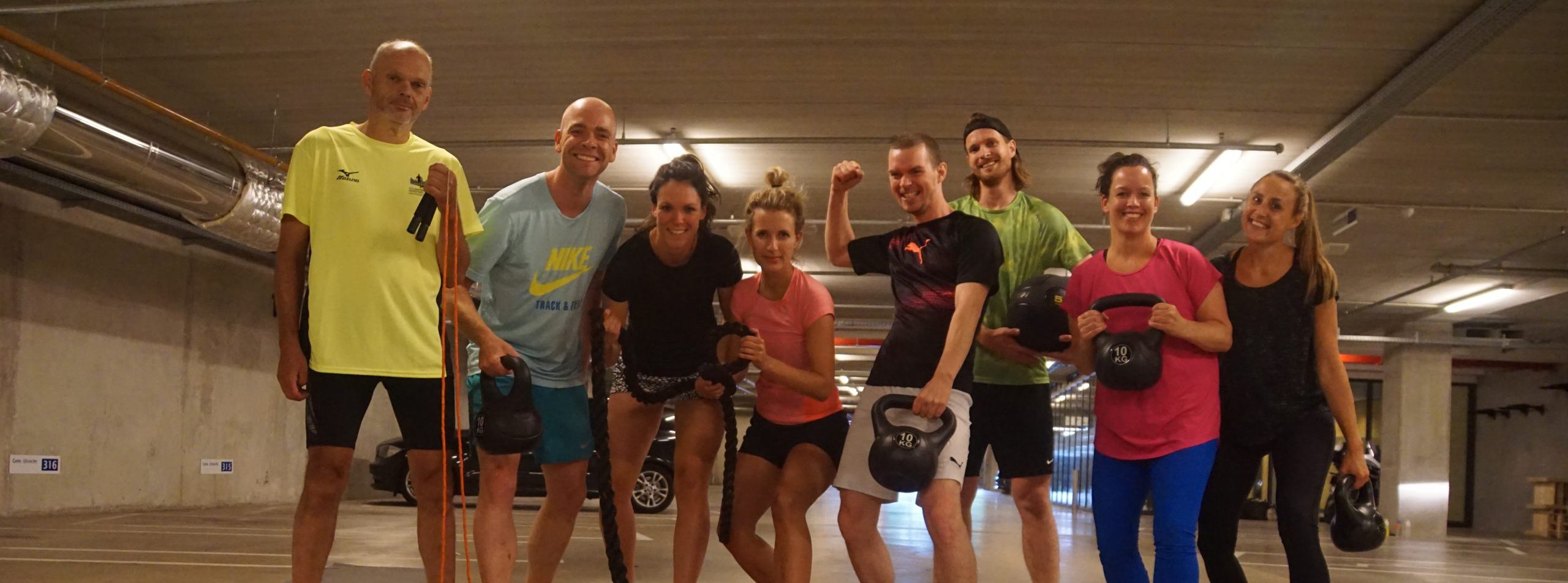 acht collega’s tijdens een bootcamp les die in de parkeergarage van het stadskantoor met sport materialen zoals matjes, kettle bells staan. 