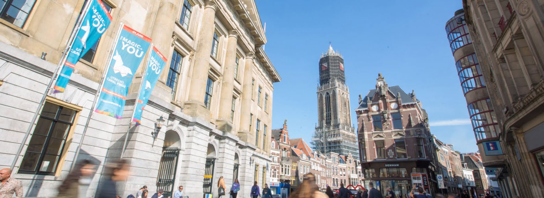 stadhuis van Utrecht met aan de voorkant fietsers en wandelaars. Op de achtergrond is de domtoren te zien en een aantal winkelpanden.