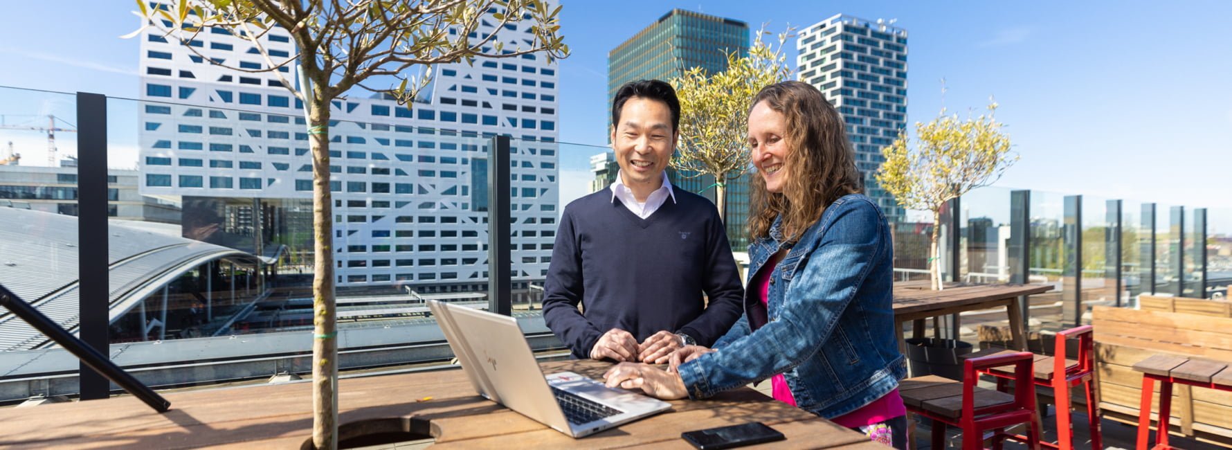 Twee medewerkers van de afdeling inkoop op een dakterras achter de computer