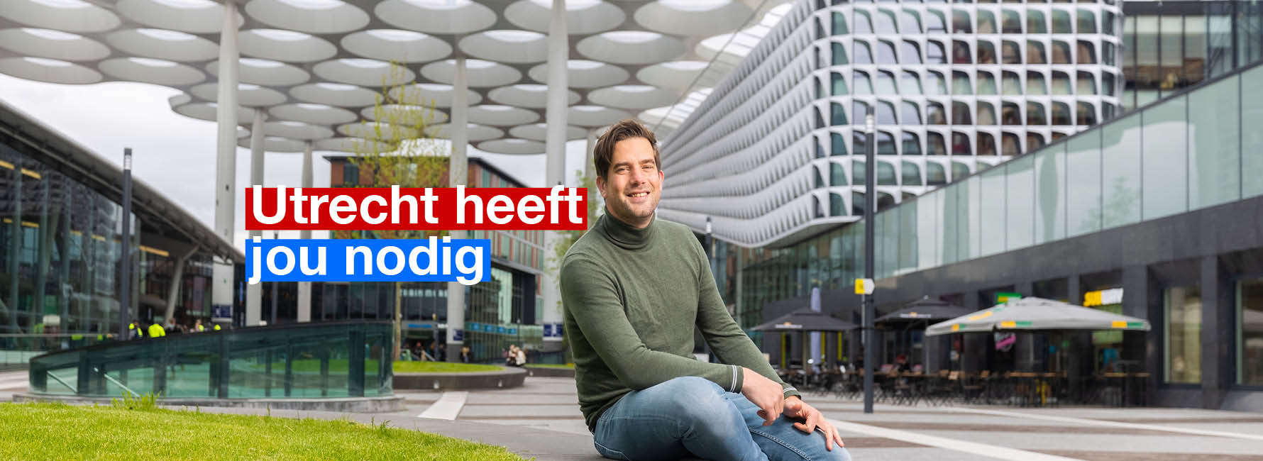 Een man zit op het stationsplein. In beeld staat de tekst Utrecht heeft jou nodig.