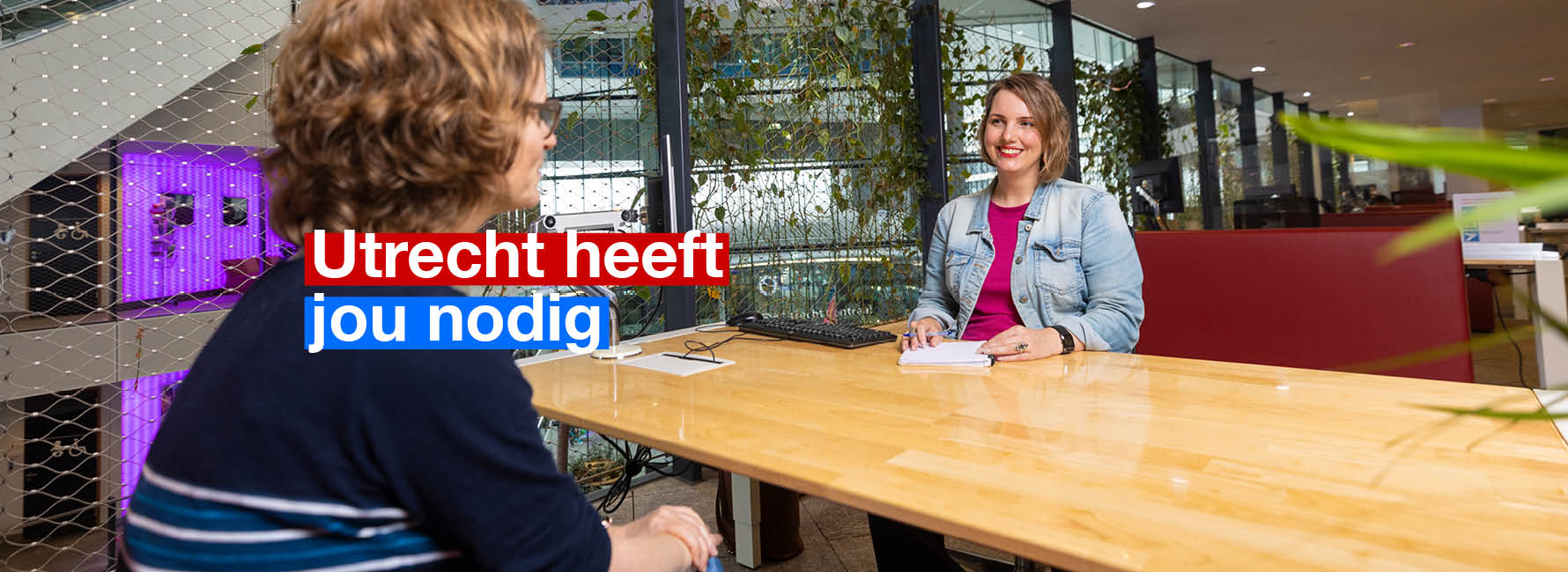Twee mensen aan een tafel in het stadskantoor. In beeld staat de tekst Utrecht heeft jou nodig.