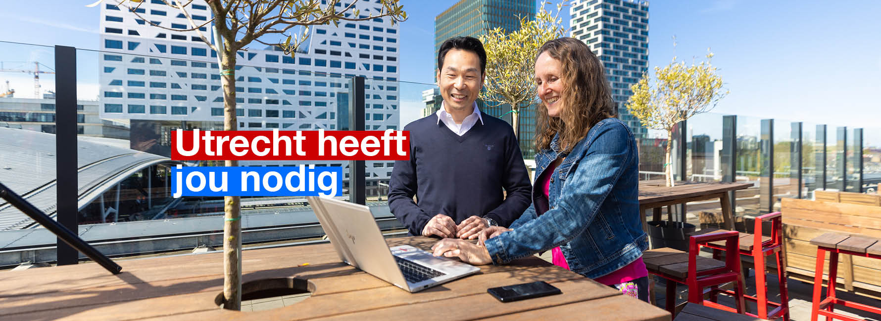 Twee mensen staan op een dakterras met een laptop. In beeld staat de tekst Utrecht heeft jou nodig.