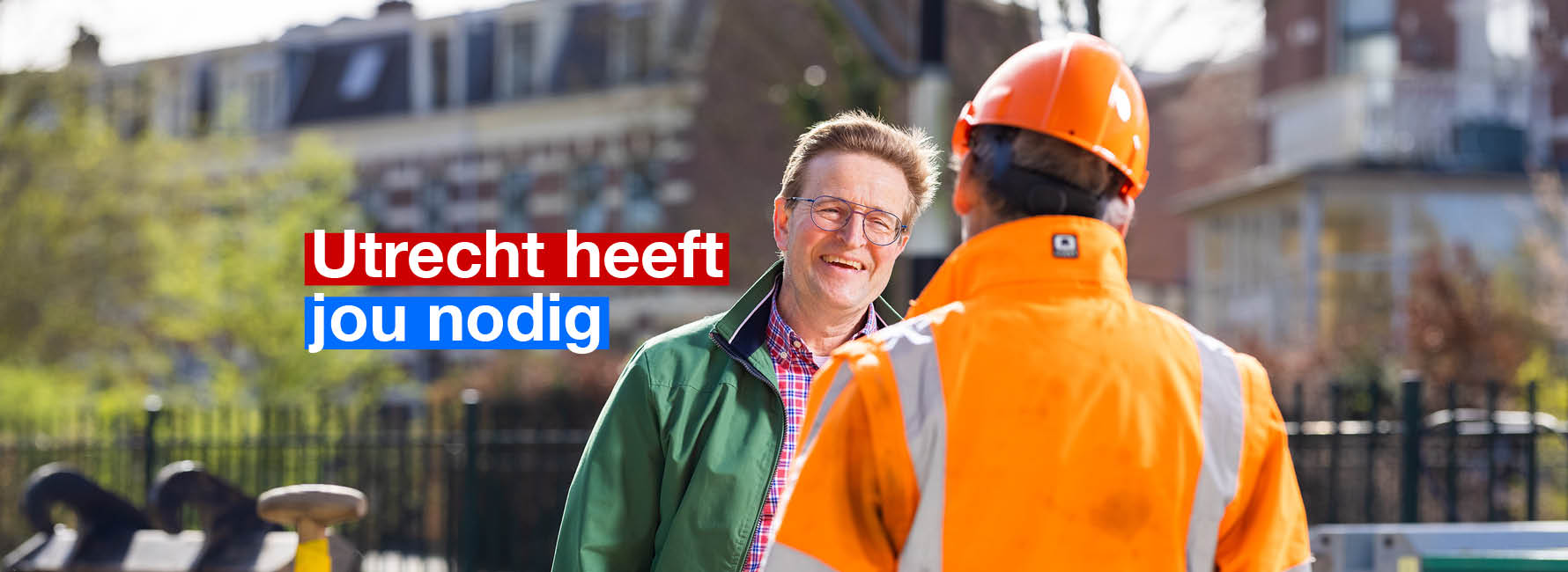 Een man met een oranje jasje en helm staat te praten met een andere man. In beeld staat de tekst Utrecht heeft jou nodig.