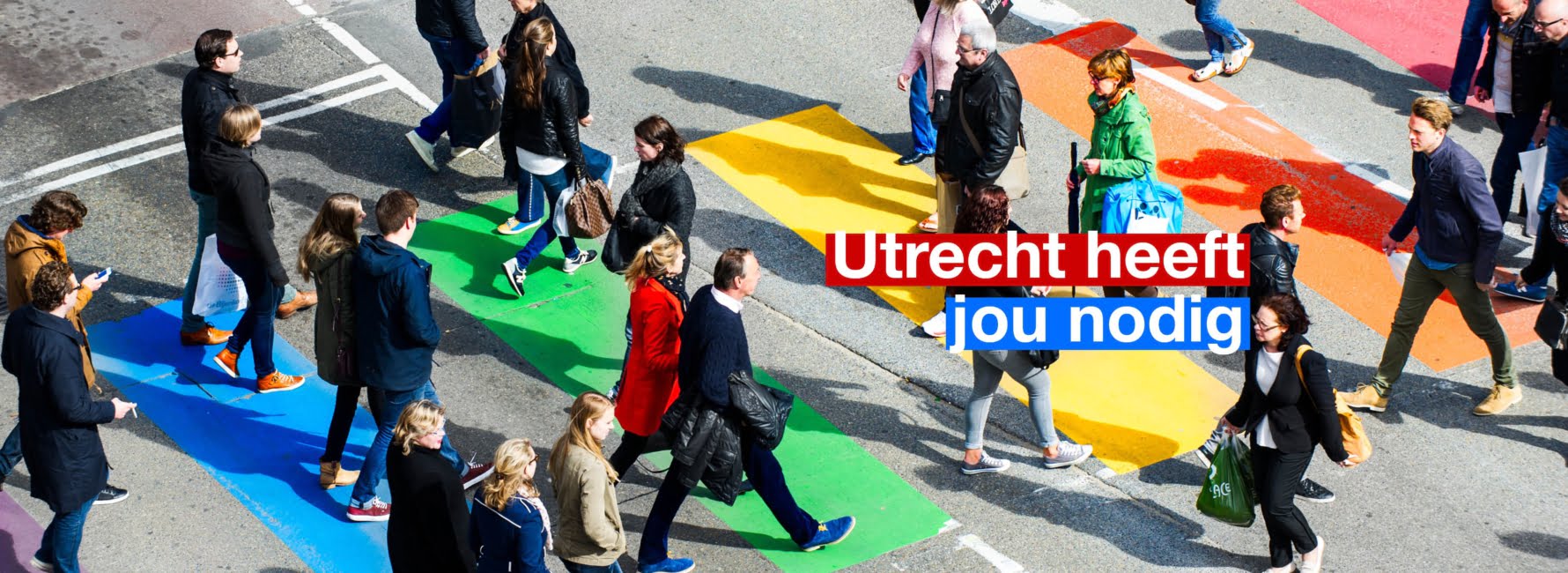 Mensen lopen over een regenboog zebrapad. In beeld staat de tekst Utrecht heeft jou nodig.