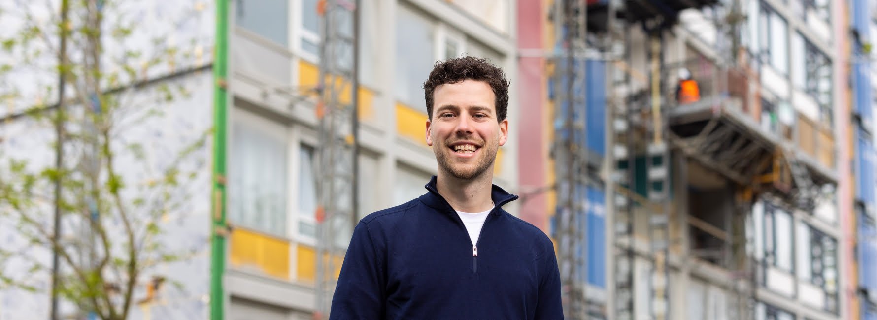 Een man voor een flatgebouw waaraan wordt gewerkt.
