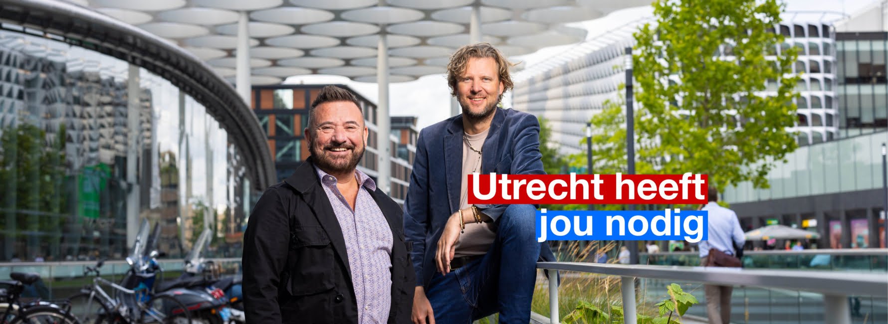 Twee collega's staan naast Utrecht Centraal Station, met op de achtergrond het bollendak. In beeld staat de tekst: Utrecht heeft jou nodig.