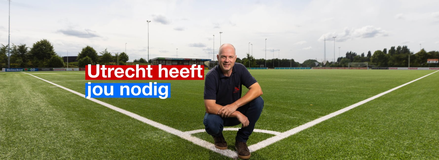 Een medewerker van een sportpark staat gehurkt aan de rand van een voetbalveld. In beeld staat de tekst: Utrecht heeft jou nodig.