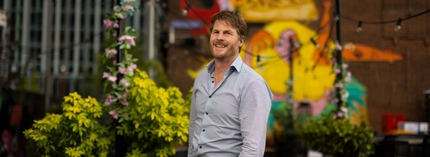 Een medewerker staat voor een muur met muurschildering.