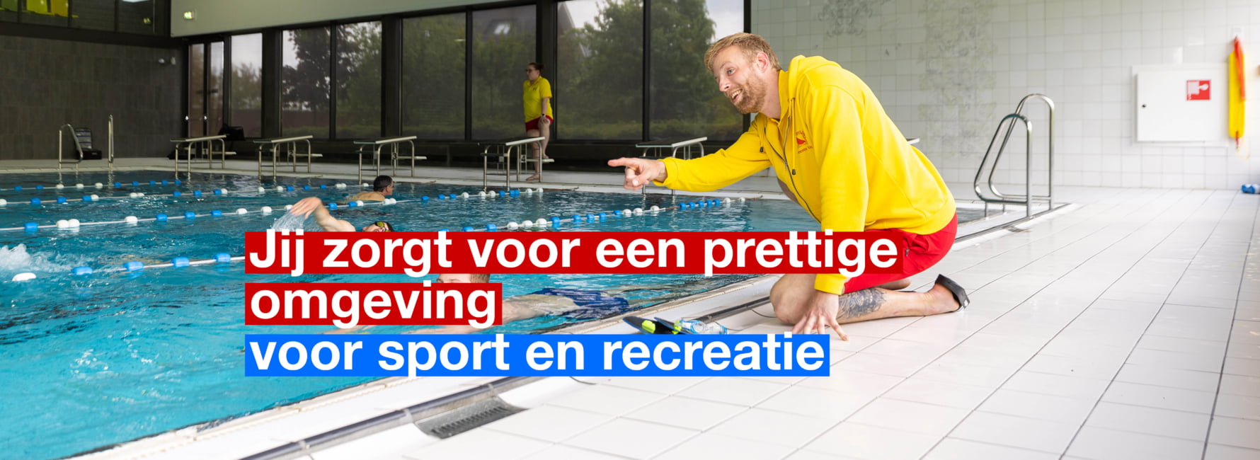 Een zweminstructeur met een geel vest zit op zijn knieën naast het zwembad. Hij geeft een instructie door te wijzen.