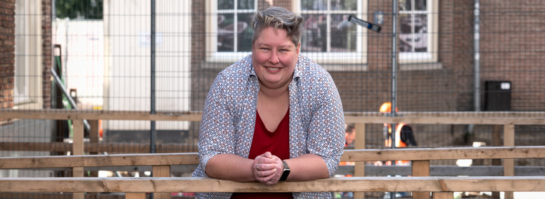 Technisch adviseur staat voorover geleund op een houten balustrade. Op de achtergrond is de grond opengebroken en zijn werkzaamheden aan de bodem en haar leidingen bezig.