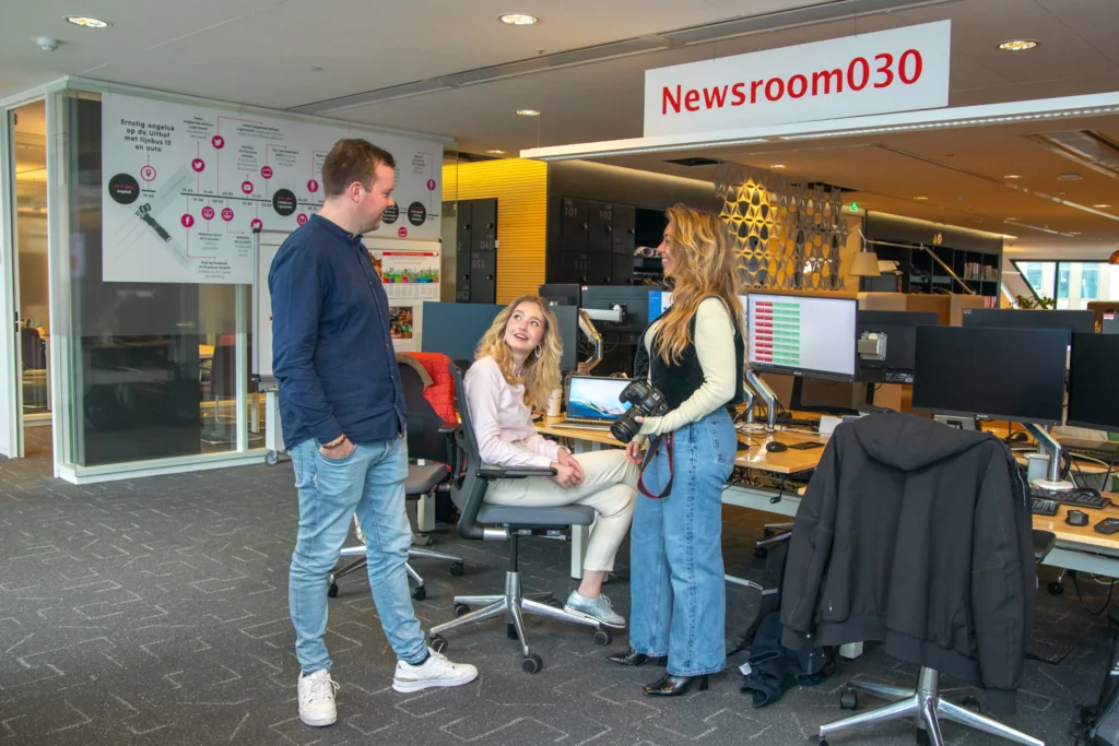 Drie medewerkers staan bij een werkplek in de NEwsroom
