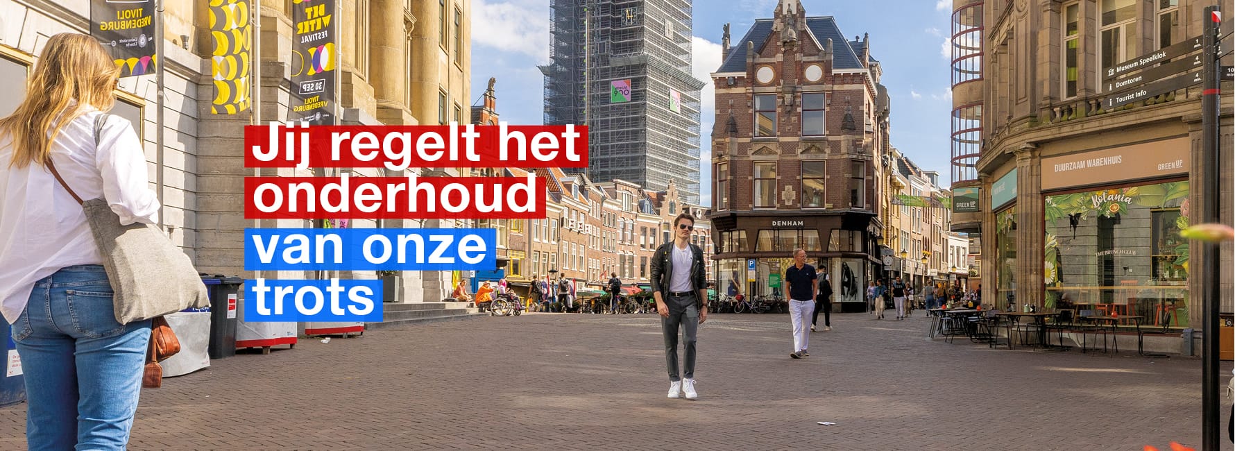 Er lopen 2 mensen voor het stadshuis in Utrecht. De domtoren is ook te zien.